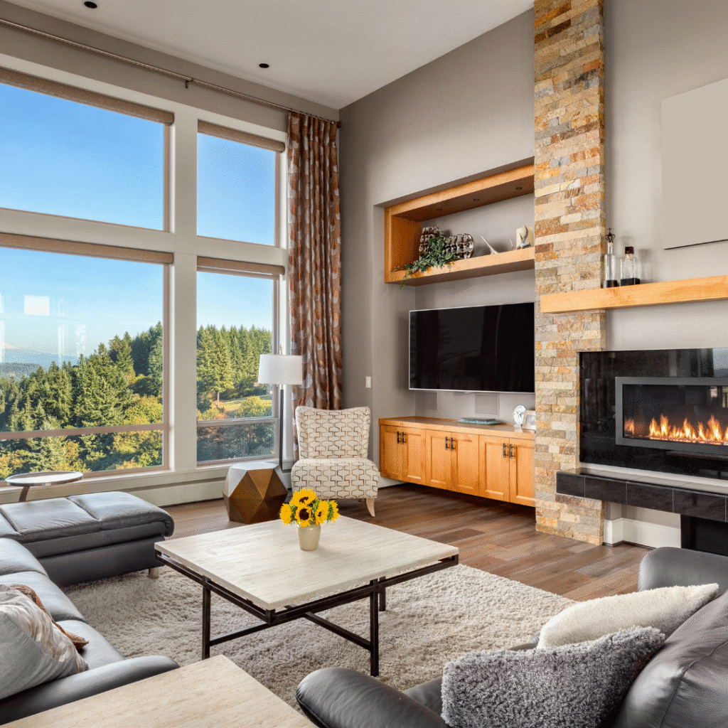 Modern living room with floor-to-ceiling windows, stone fireplace, and scenic forest view in Alberta home